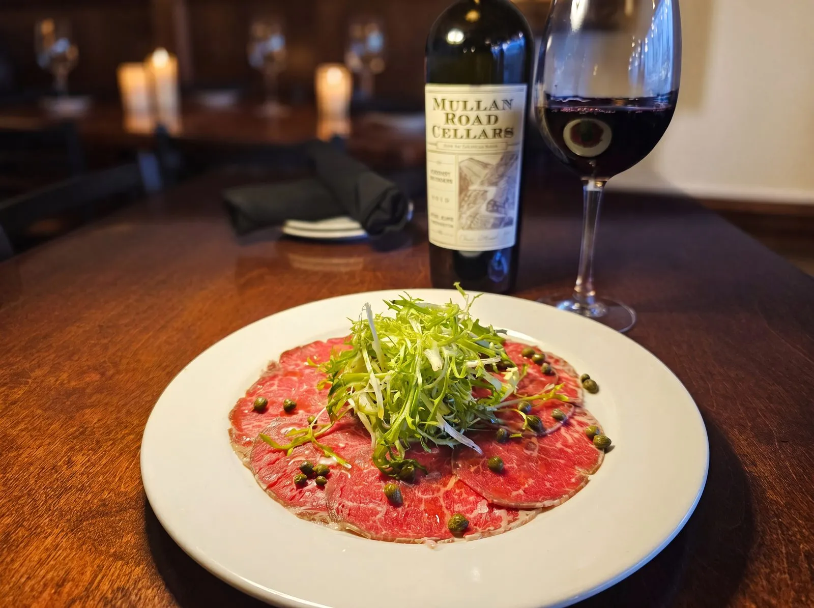 Beef carpaccio with frisee and capers in warm candlelight.